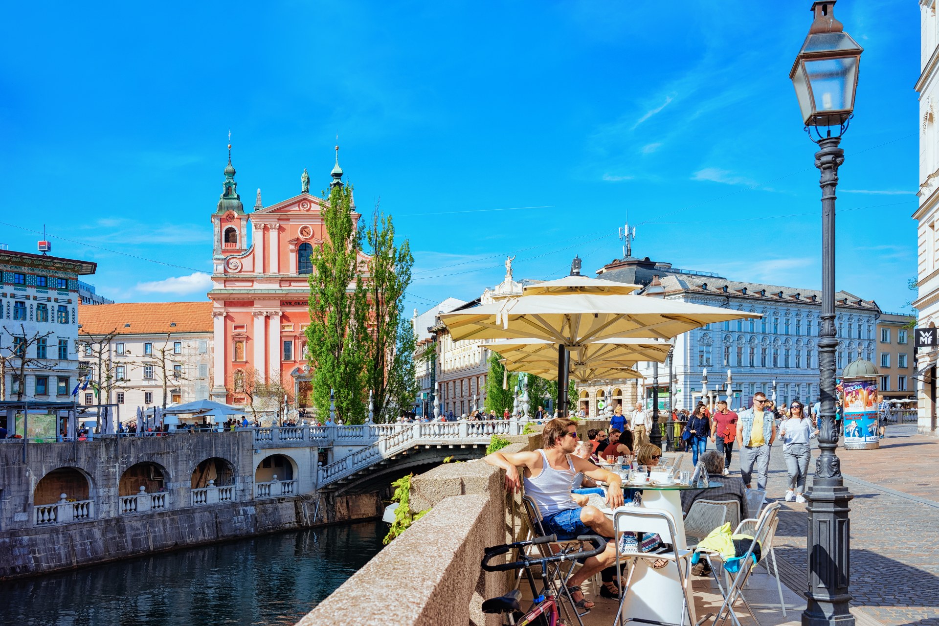 أشخاص في مقهى على الرصيف عند الجسر الثلاثي على نهر ليوبليانيتسا في ليوبليانا